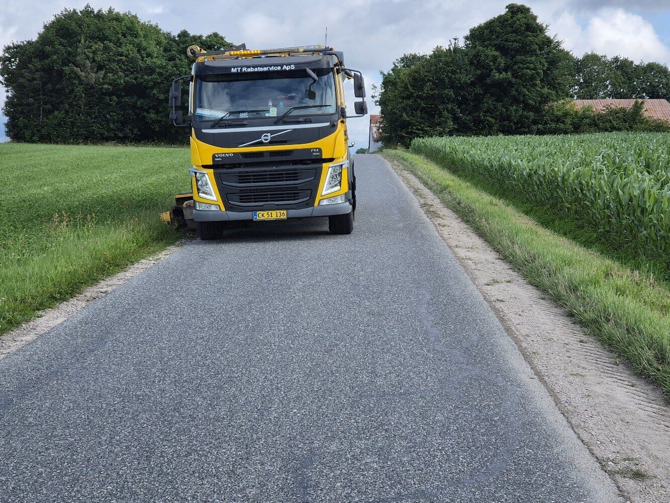Rabatbilen på en smal landevej mellem grønne marker